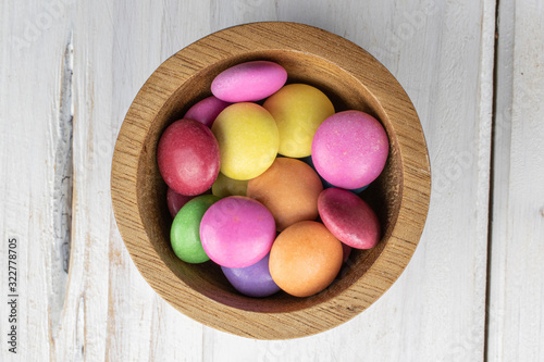 Lot of whole sweet colourful candy in bamboo bowl flatlay on white wood