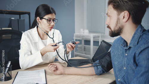 Female practitioner check patient' pressure using stethoscope manual sphygmomanometer at workplace photo