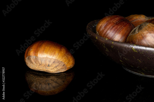 Lot of whole edible brown chestnut in glazed bowl isolated on black glass photo