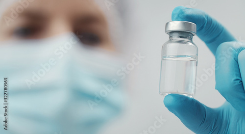 Cropped shot of doctor holding transparent glass medical vial in hand, focus on bottle photo