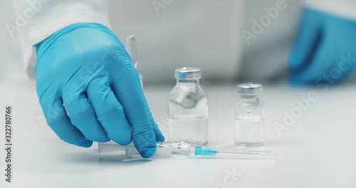Hand putting filled syringe on table next to medical glass vials with transparent liquid, cropped