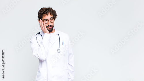 young doctor man feeling bored, frustrated and sleepy after a tiresome, dull and tedious task, holding face with hand against copy space wall photo