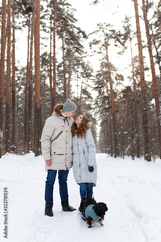 happy couple in love in warm jackets walking with their pet, with a dog, in the snow forest in winter, family trip © Елизавета Старкова
