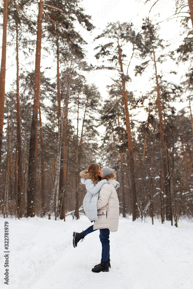 Happy lovers a guy and a girl who love each other hug, kiss, laugh, rage and walk in warm jackets in winter against the background of a snowy forest, a friendly family fun walk
