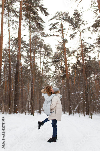 Happy lovers a guy and a girl who love each other hug, kiss, laugh, rage and walk in warm jackets in winter against the background of a snowy forest, a friendly family fun walk