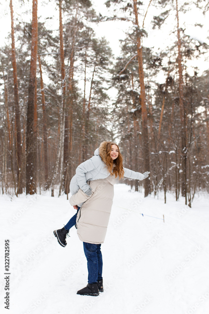 Happy lovers a guy and a girl who love each other hug, kiss, laugh, rage and walk in warm jackets in winter against the background of a snowy forest, a friendly family fun walk