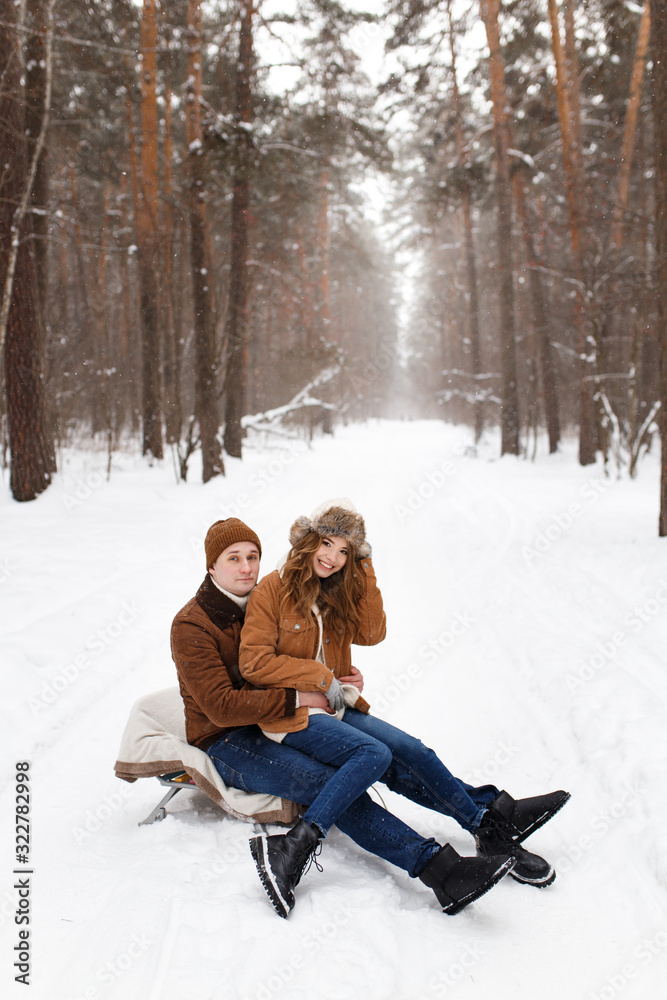Fototapeta premium Happy lovers a guy and a girl who love each other hug, kiss, laugh, rage and walk in warm jackets in winter against the background of a snowy forest, a friendly family fun walk