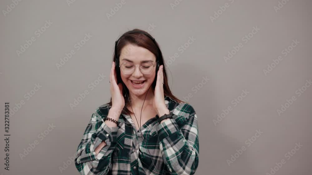 Young brunette girl blue green in checked shirt on grey background happy woman listening to music with headphones