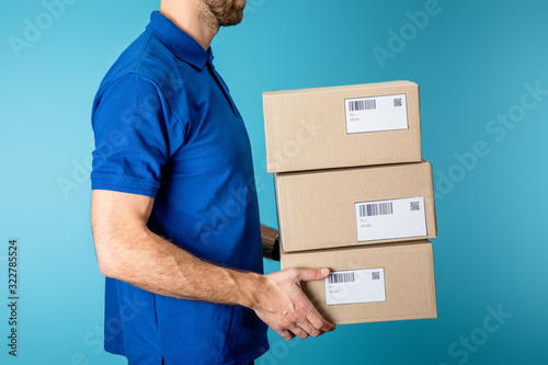 Side view of delivery man holding cardboard packages isolated on blue © LIGHTFIELD STUDIOS