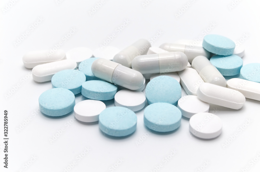 Prescription drugs, pills, capsules and tablets of different colors between white capsules and blue tablets . On white background. Selective focus.