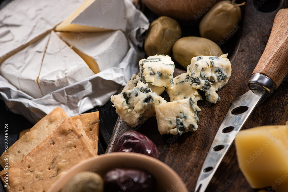 Selective focus of dorblu with knife, grana padano and olives on cutting board next to camembert and crackers