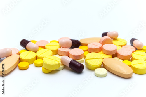 Prescription drugs, pills, capsules and vitamin C tablets of different colors all mixed in. On white background. Selective focus.