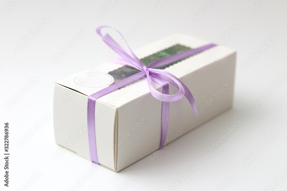 Obraz premium White cardboard box with a transparent top tied with a lilac ribbon isolated on a white background. A wonderful gift for Valentine's Day, birthday.