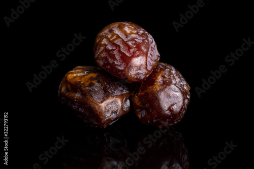 Group of three whole dry brown date fruit isolated on black glass