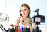 Pretty Beauty Vlogger Promote Cosmetology Product. Stunner Woman Holding Makeup Tools, Filming Technique Tips on Tripod Camera. Blond Caucasian Visagiste Work on Creative Blog Content