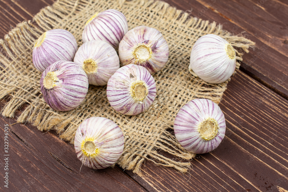 Group of nine whole fresh purple single clove garlic on natural sackcloth on brown wood Group of nine whole fresh purple single clove garlic on natural sackcloth on brown wood