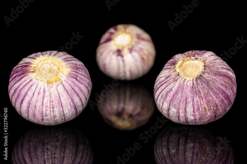 Group of three whole fresh purple single clove garlic isolated on black glass