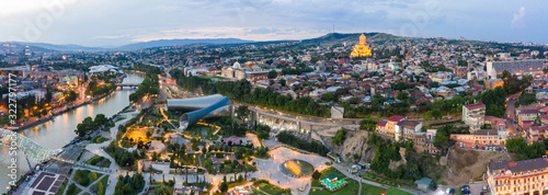 Panorama of the old town in the old district of Avlabari, Holy Trinity Cathedral and Rike Park, the Kura river reflects the evening city lights and cars traffic with blure in Tbilisi, Georgia
