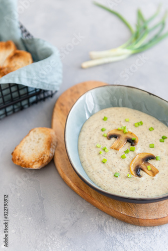 Mushroom cream soup with cream, toasts and shallot in a bowl on gray background. Delicious healthy food, dieting, keto diet