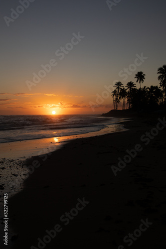 Orange sun is rising on the beach of a tropical island. Amazing sky and sun going up, palm silhouettes: a postcard from paradise. Scenic view, vacation concept.