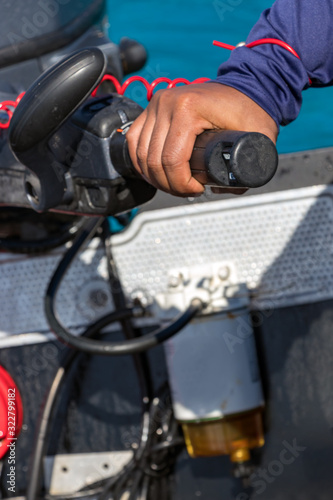 Male hand driving a inflatable boat holding the tiller of an outboard motorboat, close up, outdoors. © Ruben