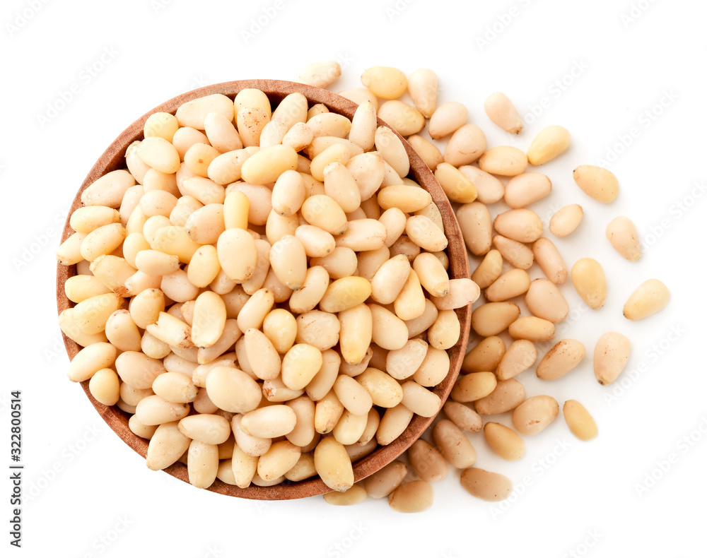 Pine nuts in a wooden plate and scattered on a white. The view of the top. Pine nuts in a wooden plate and scattered on a white. The view of the top.