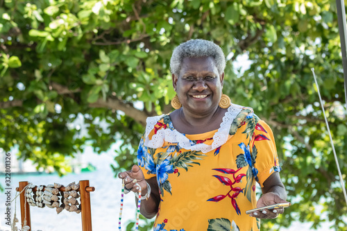 Portrait of a melanesian - australian mature woman smiling, possing at her stall holding a necklace that she has made, outdoors. photo