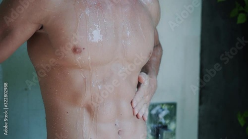 Close up of naked muscular torso of man taking shower in bathroom, slow motion