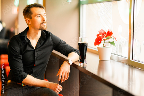 A handsome middle-aged man in a bar. The boy enjoys a dark beer. There is a pleasant atmosphere for fun.