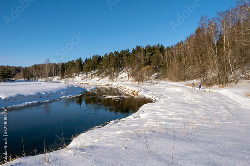 Landscape with a small river and two skiers on a winter sunny day and blue sky. © Valery Smirnov
