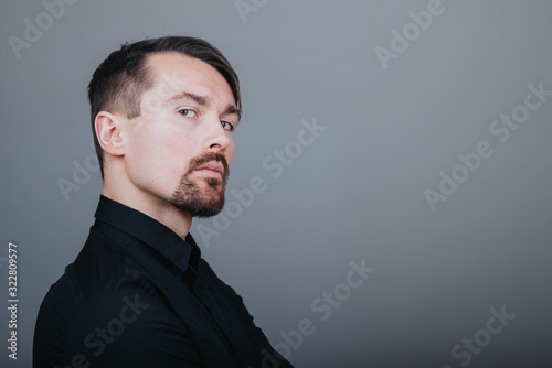 Photo of a handsome man with a coolly stylized scrub and hairstyle. Photo taken in a photo studio on a gray background. The man tries to express his emotions with gesticulation and mimics.
