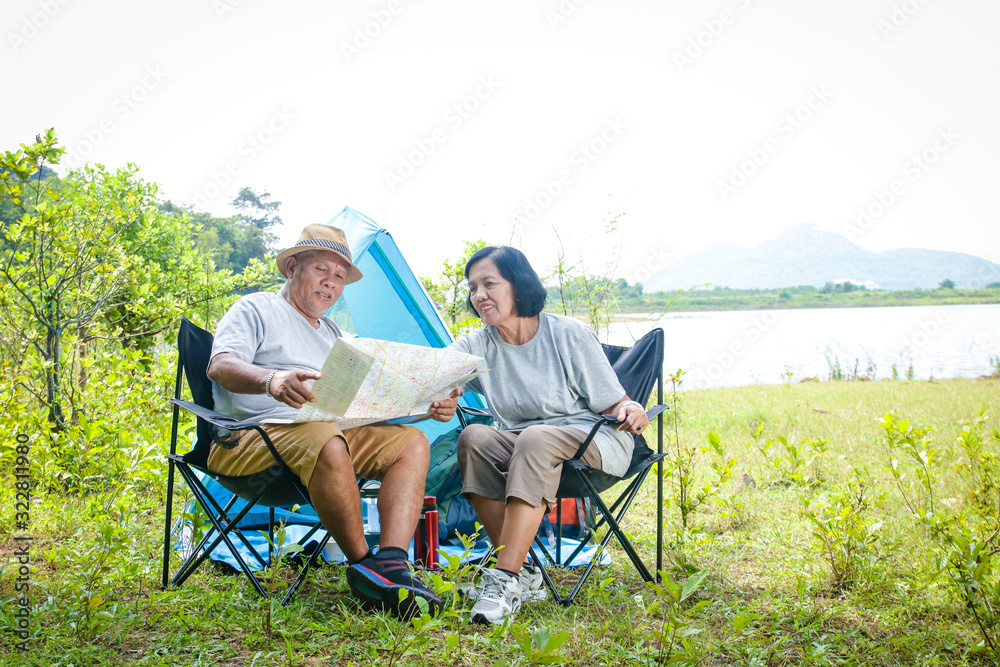 Happy asian senior couple Camping at the waterfront, sitting on a chair, view tourist map, with copy space. Happy asian senior couple Camping at the waterfront, sitting on a chair, view tourist map, with copy space.