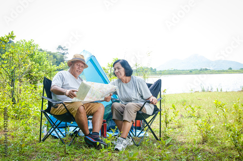 Happy asian senior couple Camping at the waterfront, sitting on a chair, view tourist map, with copy space.