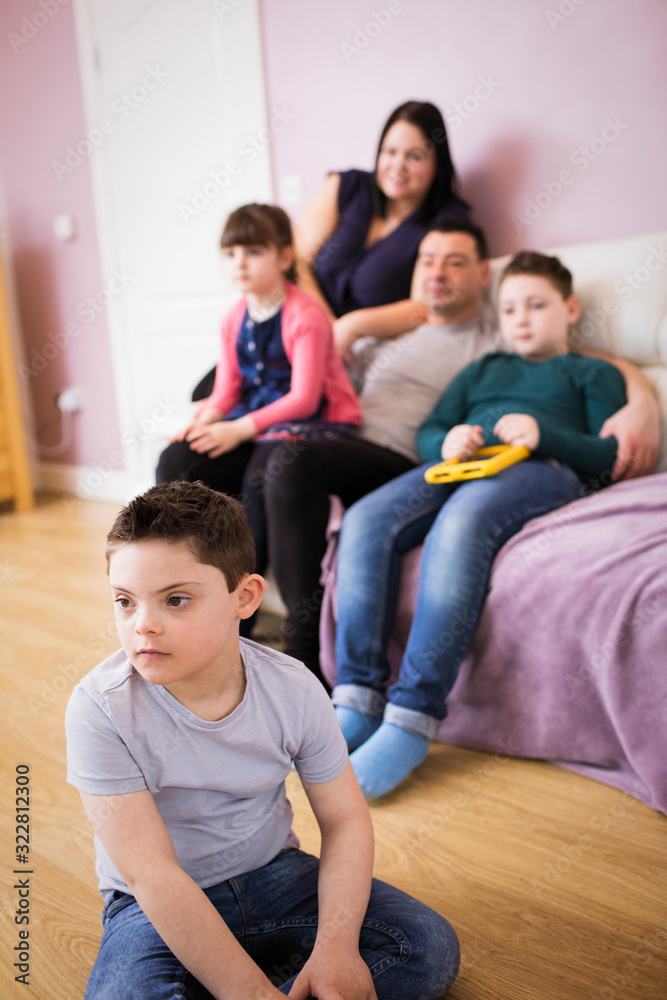 Boy with Down Syndrome watching TV with family in living room Boy with Down Syndrome watching TV with family in living room