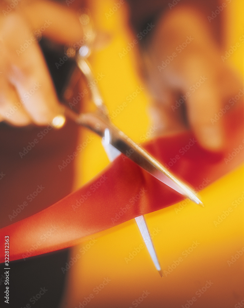 A hand with scissors cutting a red ribbon. A hand with scissors cutting a red ribbon.