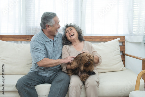 Happy elderly senior asian couple sit on sofa together with pet therapy in nursing daycare,Retired man and woman holding dog while sitting on couch in living room at home.