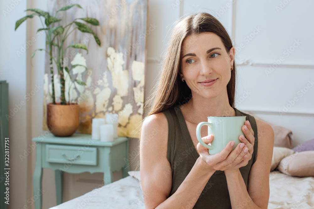 Beautiful lifestyle picture of woman drinking from cup and smiling in boho light interior Beautiful lifestyle picture of woman drinking from cup and smiling in boho light interior