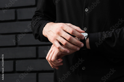 stylish man with wristwatch near wall checks what hour