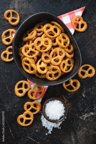 Bowl of pretzels with sea salt over dark brown stone surface, flatlay, view from above