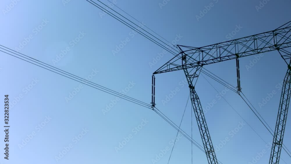 Looking up steel pylon with electric power lines against clear blue sky with sun Looking up steel pylon with electric power lines against clear blue sky with sun