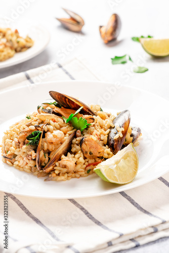 Seafood risotto in a white plate on the served table. Risotto with shrimp, tomatoes, parsley and mussels in shells. Tasty and healthy Mediterranean cuisine.