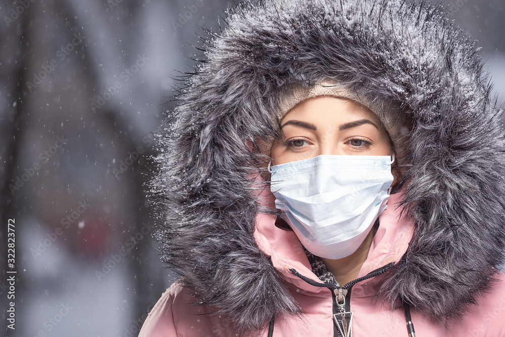 Portrait of woman in pink walking down the street in winter under snowfall in a protective mask to protect against infectious diseases. Protection against colds, flu, air pollution. Health concept Portrait of woman in pink walking down the street in winter under snowfall in a protective mask to protect against infectious diseases. Protection against colds, flu, air pollution. Health concept