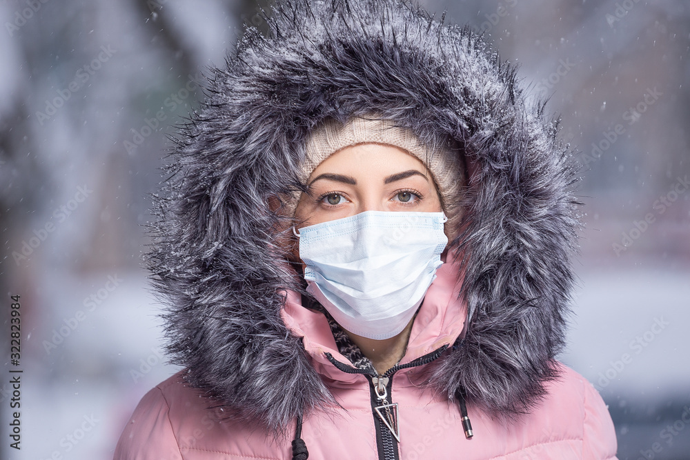 Portrait of woman in pink walking down the street in winter under snowfall in a protective mask to protect against infectious diseases. Protection against colds, flu, air pollution. Health concept Portrait of woman in pink walking down the street in winter under snowfall in a protective mask to protect against infectious diseases. Protection against colds, flu, air pollution. Health concept
