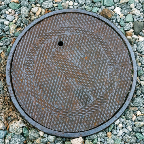 Rusty manhole cover with gravel and rocks.