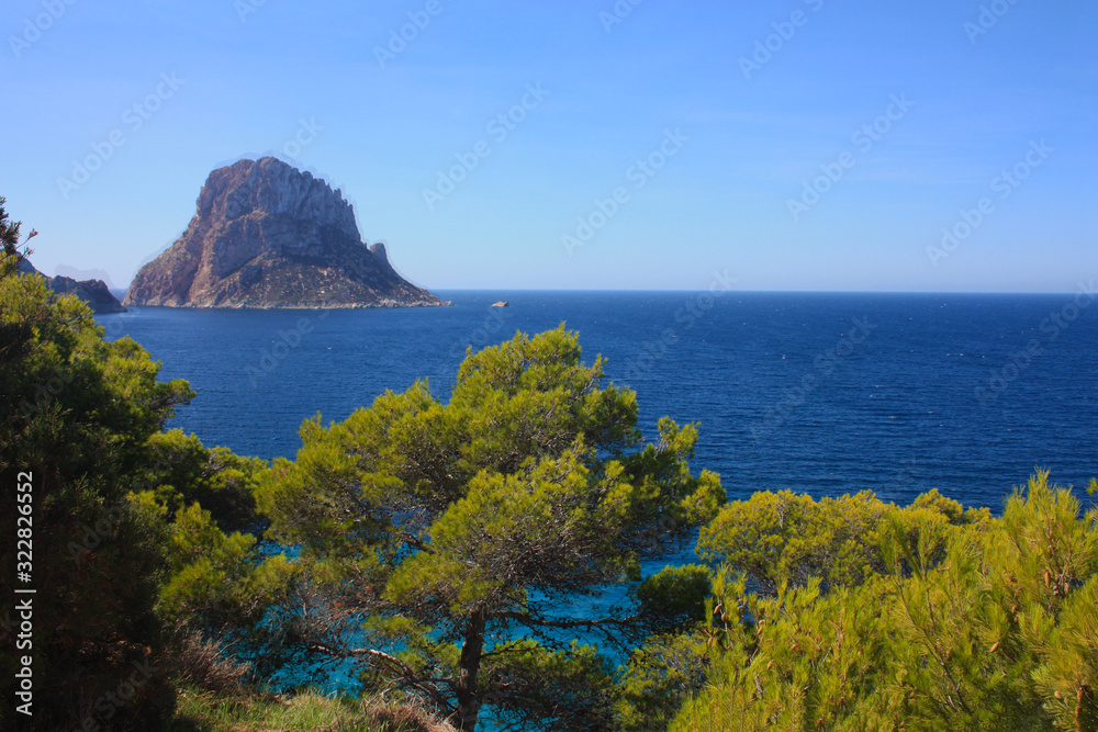 The solitary islet of Es Vedra in contrast against the blue sea of ​​Ibiza immersed in the green and arid wild nature