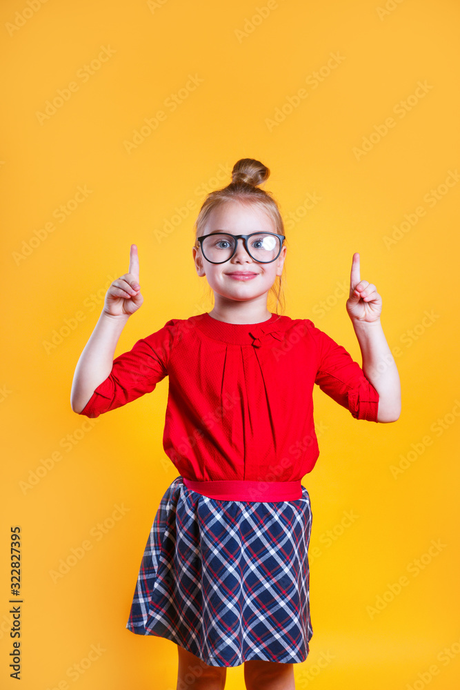 Little schoolgirl in glasses with raised index fingers on color background Little schoolgirl in glasses with raised index fingers on color background