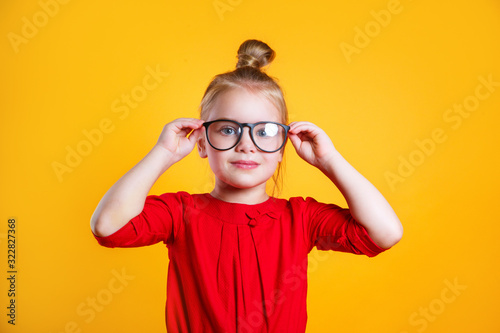 Portrait of smart little girl with glasses on yellow background
