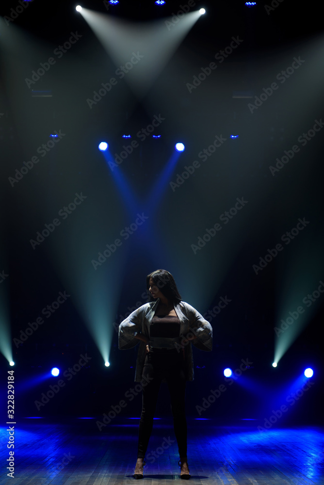 Obraz premium Girl in black suit performing on stage with bright blue background