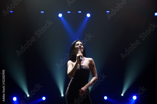 Singer perform on stage of nightclub in front of bright screen. Dark background, smoke, concert spotlights
