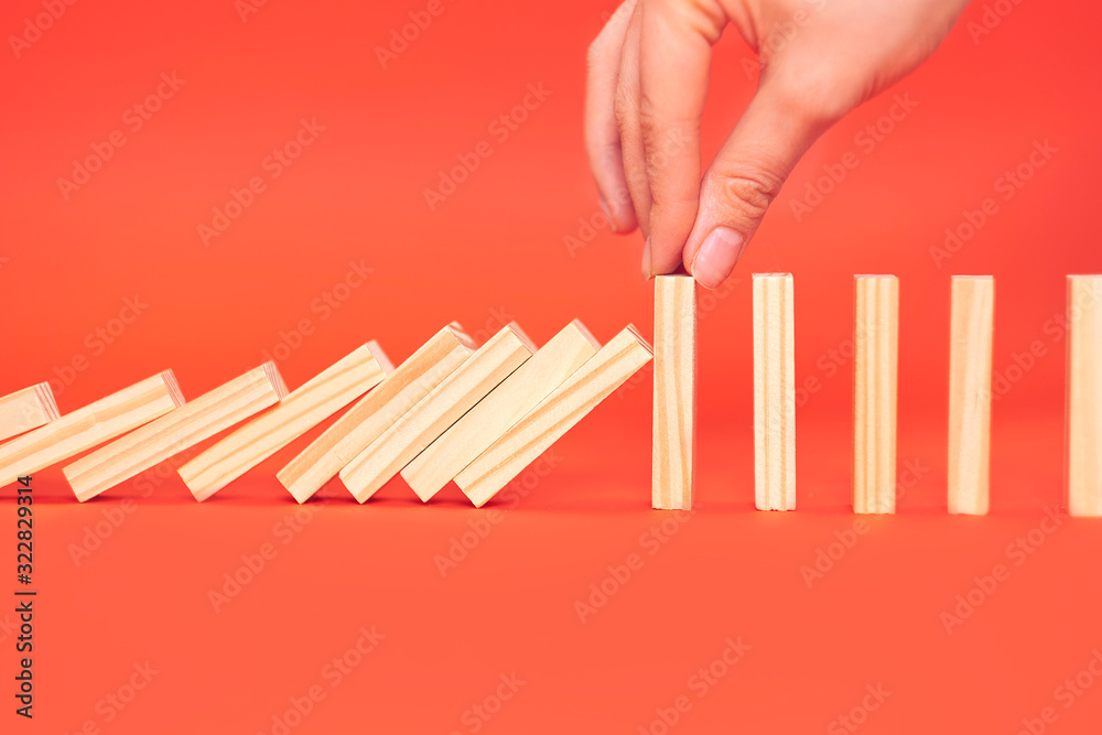 hand finger stops falling wooden dominoes, red background, domino principle, business concept hand finger stops falling wooden dominoes, red background, domino principle, business concept